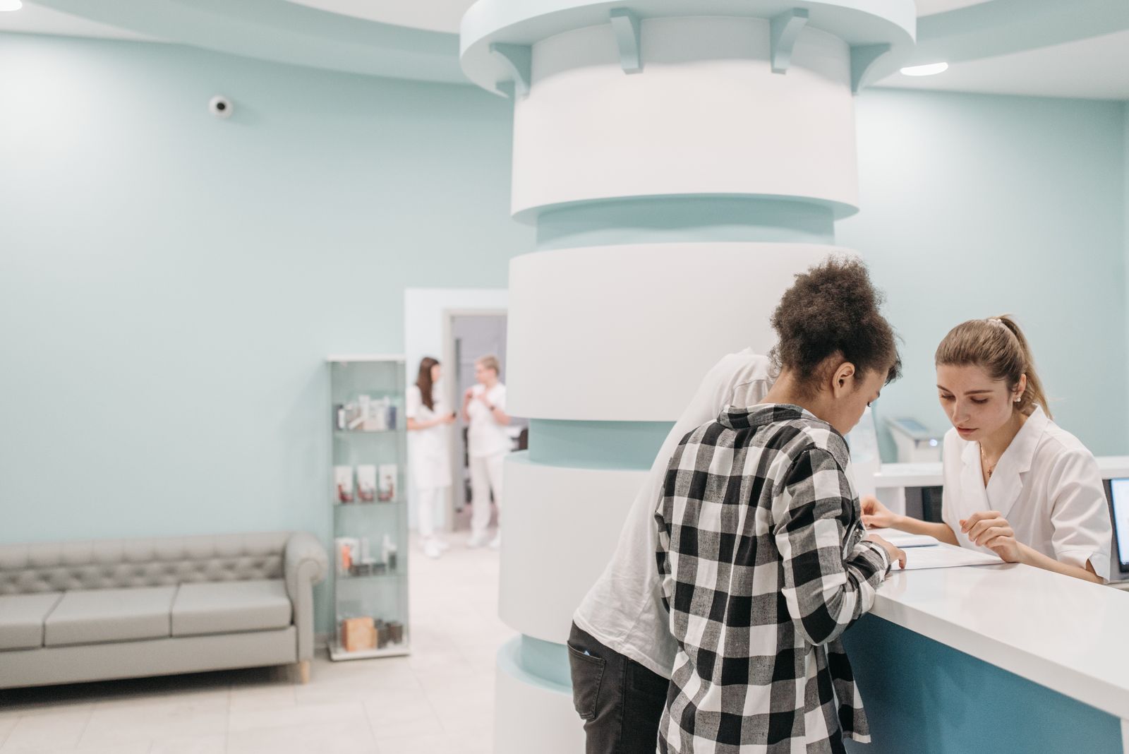 A bright, pale-green clinic reception with staff helping two clients at the desk