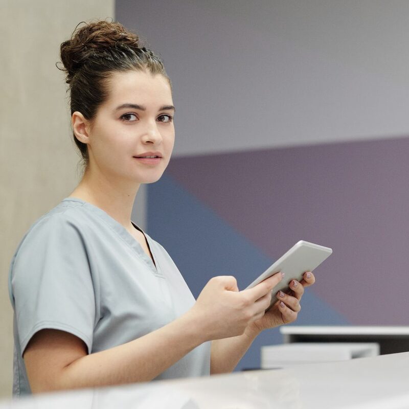 Renee Whitlock in lavender scrubs at the front desk with a tablet